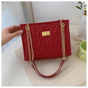 Close-up of red quilted handbag with gold lock and chain strap on a white table