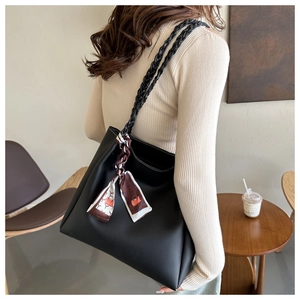 Detail of a black leather tote with woven handles and a decorative printed silk scarf