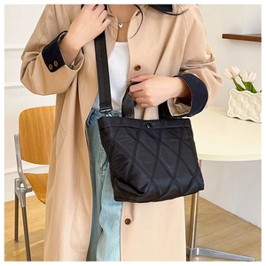 Détail du sac seau noir matelassé avec large bandoulière porté par un mannequin