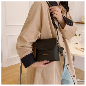 Detail of black litchi texture crossbody bag with thick woven strap and pony charm