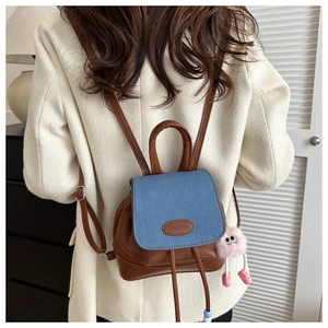 Detail of a brown leather and blue denim mini backpack with a pink plush monster charm