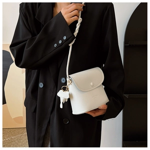 Close-up of white pebble leather crossbody bag with woven strap and elephant charm