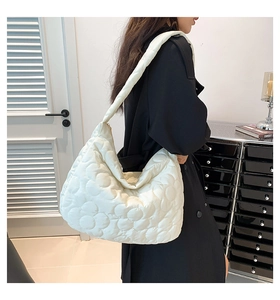 Detail einer großen cremefarbenen Stepp-Schultertasche mit Blumenmuster an einem Model