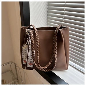 Macro view of textured brown tote bag featuring braided straps and patterned silk scarf