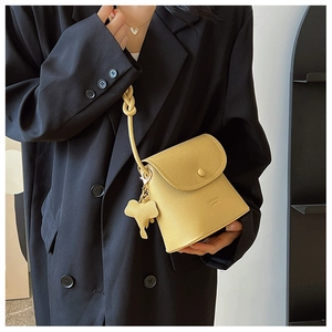 Detail of yellow pebbled leather crossbody bag with knot strap and elephant charm