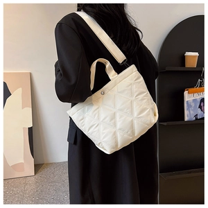 Sac seau matelassé blanc avec bandoulière large porté sur un blazer noir élégant