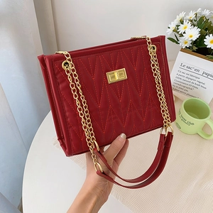 Red quilted shoulder bag with gold chain strap and turn-lock closure in lifestyle setting