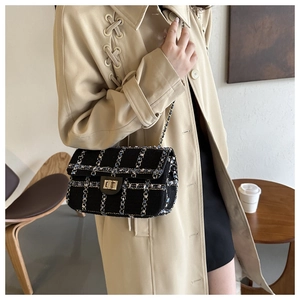Close-up van zwarte tweed crossbody tas met gouden ketting op een beige trenchcoat