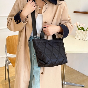 Quilted black nylon tote bag with crossbody strap shown by model in minimalist interior