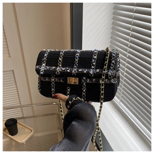 Detail van zwarte tweed crossbodytas met gouden draaisluiting en geweven kettingriem