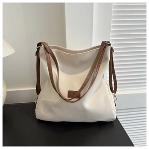 Close-up of cream canvas tote bag featuring brown leather handles and 'M' logo detail