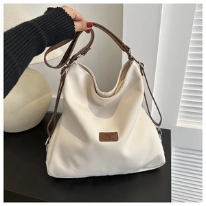 Detail of minimalist cream canvas tote bag featuring brown leather logo and handles