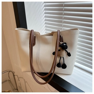Close-up of cream leather tote bag with brown straps and cute sheep pendant by window