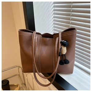 Detail of brown tote bag featuring contrast white stitching and a plush sheep charm