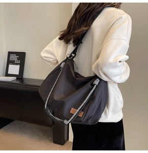 Detail of black large capacity tote bag with woven shoulder strap and brand patch