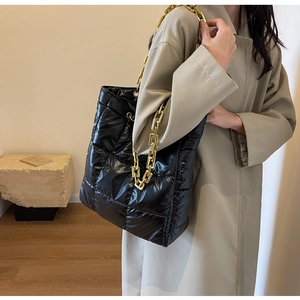 Close-up of black quilted bucket bag with chunky gold chain strap on a model