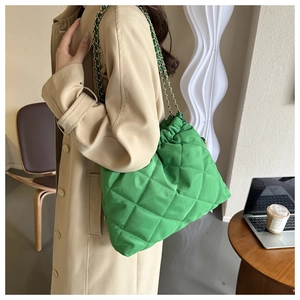 Detail van een felgroene gewatteerde emmertas met ketting bij een beige trenchcoat