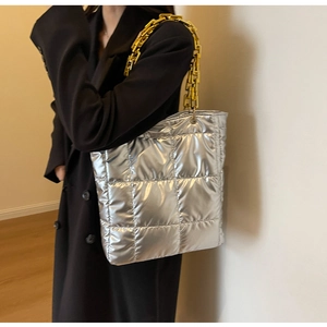 Silver quilted tote bag with chunky gold chain strap shown on black coat model