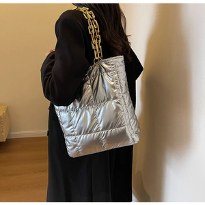 Silver quilted tote bag with chunky gold chain strap shown on model shoulder