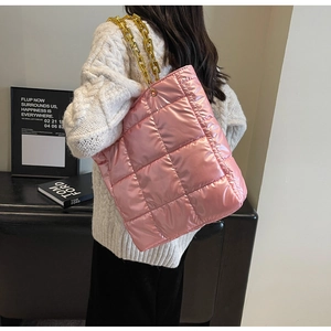 Detail of pink glossy quilted tote bag with chunky gold chain strap worn by a model