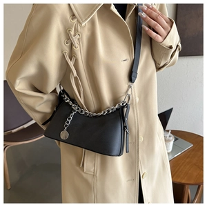 Side view of a black leather crossbody bag with silver chain detail on a beige trench coat