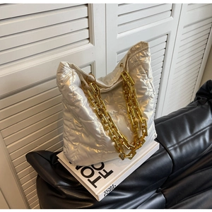 Close-up of white quilted bubble tote bag with chunky gold chain strap on dark leather