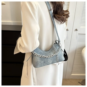 Detail of light blue denim crescent bag with silver metal chain on female model