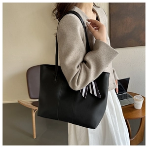 Detail of a large black leather tote bag with a striped silk scarf on a model