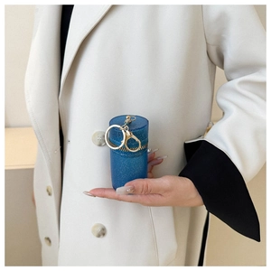 Close-up of a blue glitter mini cylinder chain bag held by a model in a beige coat
