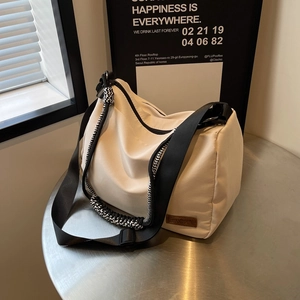 Chic beige crossbody tote bag with black wide straps and braided handle on a metal table