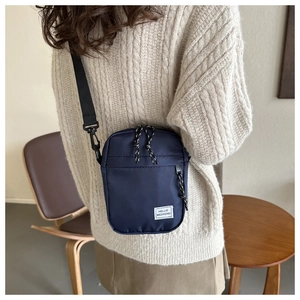 Dettaglio borsa a tracolla in nylon blu navy con etichetta HELLO WEEKEND su maglione beige