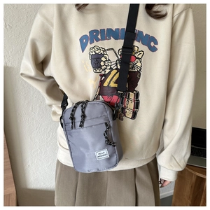 Close-up of gray nylon crossbody bag with HELLO WEEKEND label on beige sweater