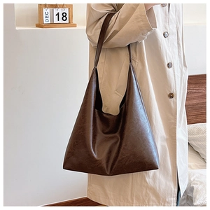 Détail d'un grand sac cabas marron foncé en similicuir vintage sur un trench-coat beige