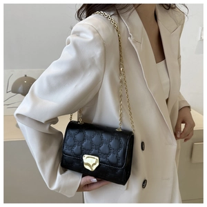 Dettaglio borsa a tracolla trapuntata nera con catena dorata e fibbia su blazer beige