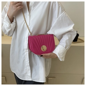Detail of magenta shell-textured saddle bag with golden clasp on white shirt
