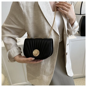 Detail of black pleated saddle bag featuring a gold seashell clasp and fine chain strap