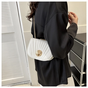 Detail view of white saddle bag with golden shell-shaped clasp and vertical quilting