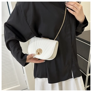 Detail of white leather saddle bag with pleated texture and gold chain on model