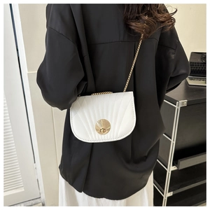 Detail of white shell-textured saddle bag with golden shell buckle and chain strap