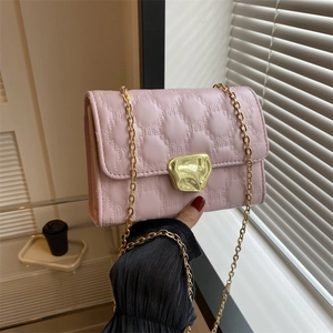 Borsa a tracolla trapuntata rosa con chiusura dorata e catena tenuta dalla modella