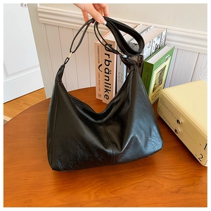 Detail of black leather hobo bag with vertical stitching on wooden table with books