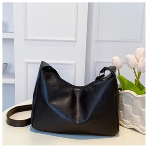 Detailed view of black crescent shoulder bag with oil wax texture and wide strap on white stand