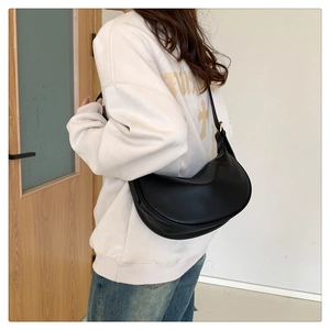 Side view of soft black leather half-moon shoulder bag worn by a model in a minimalist setting