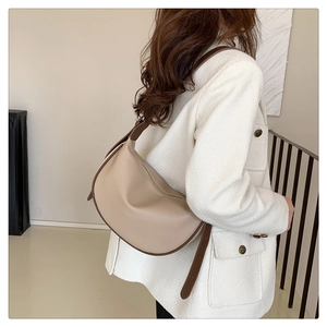 Detail of beige crescent crossbody bag with brown trim on model wearing white tweed