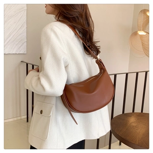Detail of a brown leather half-moon hobo bag with adjustable strap on a white coat