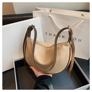 Detail view of the soft beige crescent bag with brown trim and gold metallic hardware