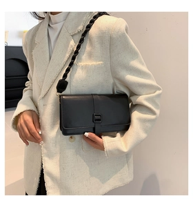 Dettaglio borsa a tracolla in pelle nera con tracolla intrecciata su giacca tweed