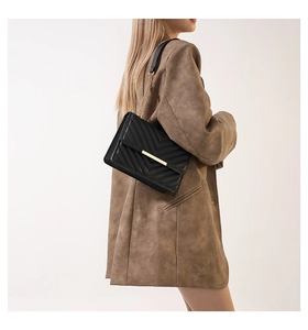 Detailed view of black quilted faux leather bag with gold chain strap on model