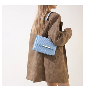 Close-up of light blue quilted crossbody bag with gold chain strap and metal clasp