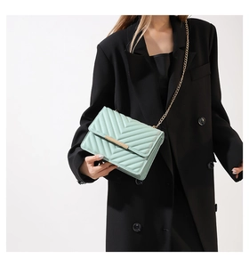 Detail of mint green quilted chain shoulder bag on model with elegant gold hardware